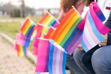 People sitting on a bench holding different flags for the protest defending the LGBTQ rights