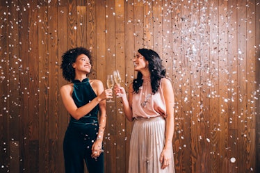 Two young woman posing in their New Year's Eve outfits clinking champagne.