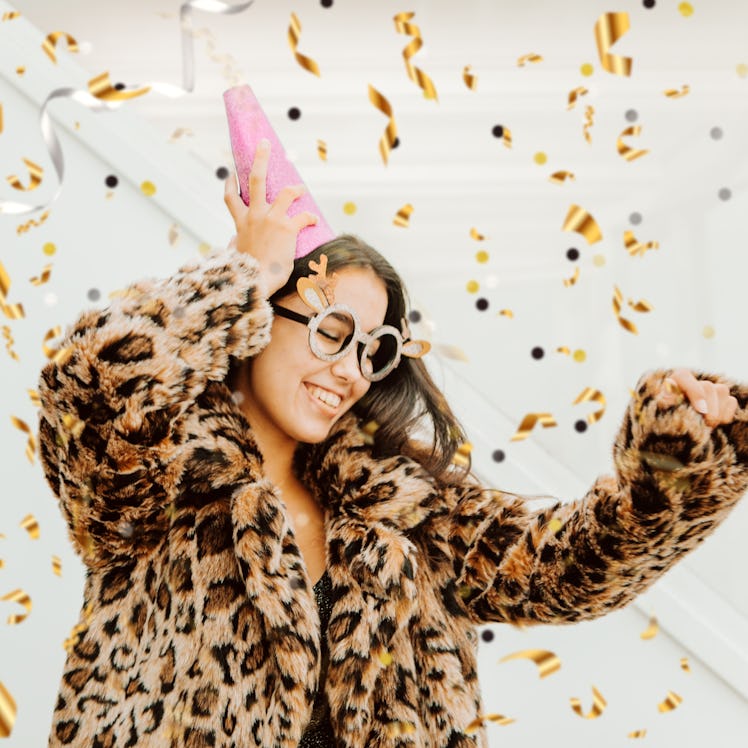 A young woman dancing in a gorgeous New Year's Eve dress and leopard print coat, thinking of the bes...