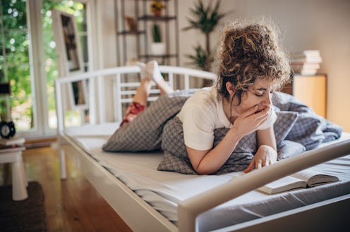 A woman lies in bed at home, yawning, wondering why caffeine doesn't wake me up.