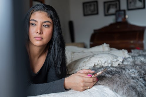 Young latin woman from bogota Colombia between 20 and 24 years old, lying in bed enjoying her cell p...