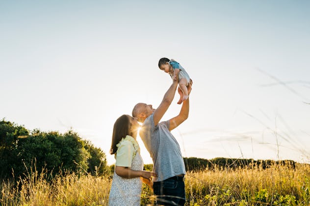 Father throwing up to the air and playing with his three months old son on the countryside