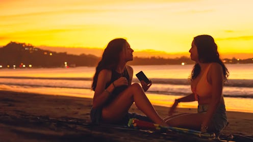 Two beautiful young women with long, wavy hair, playing and taking selfies at beach at sunset in Pla...