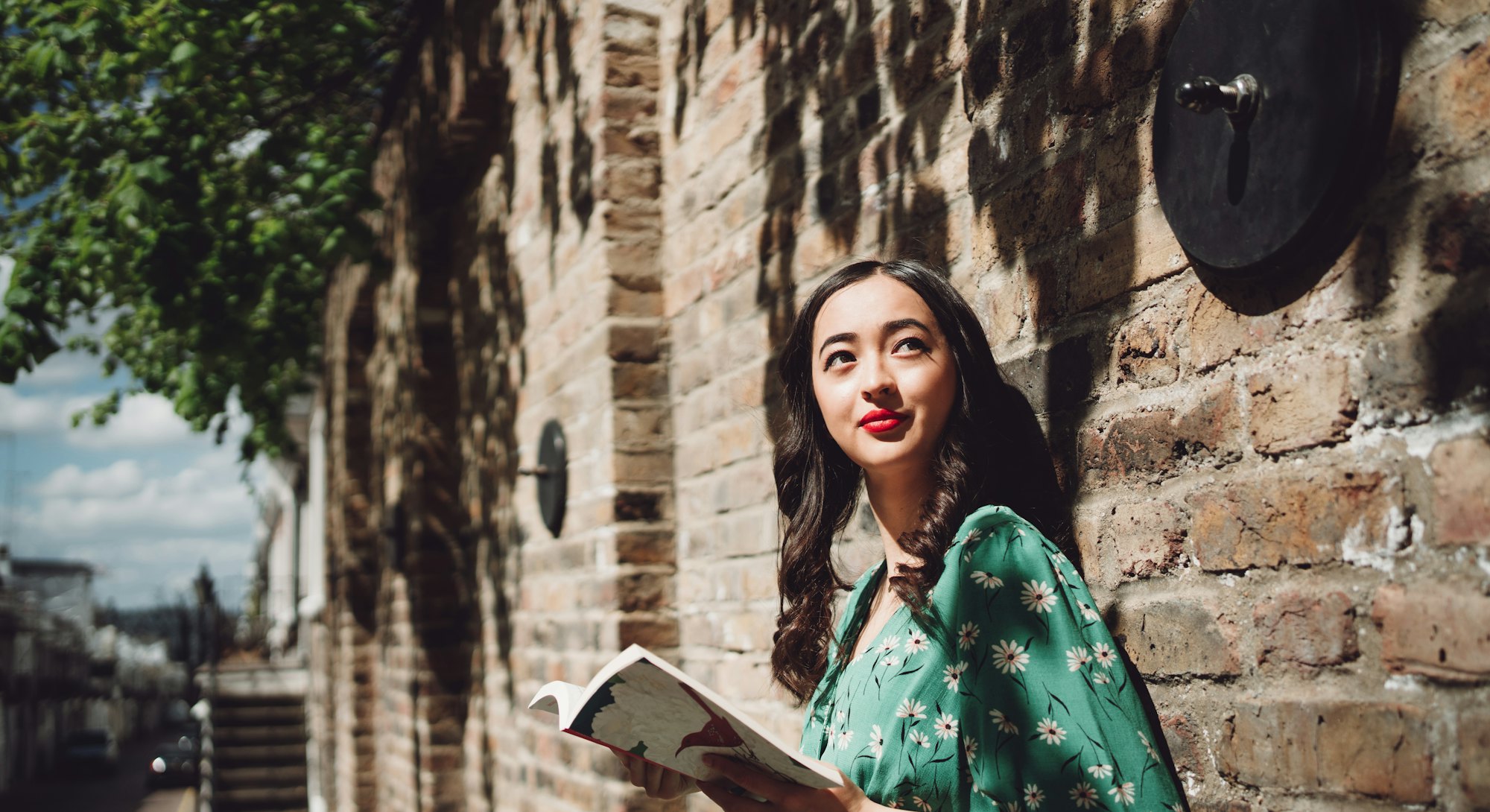 Cheerful beautiful young Asian Brazilian mixed women looking up to the sky while holding a novel on ...