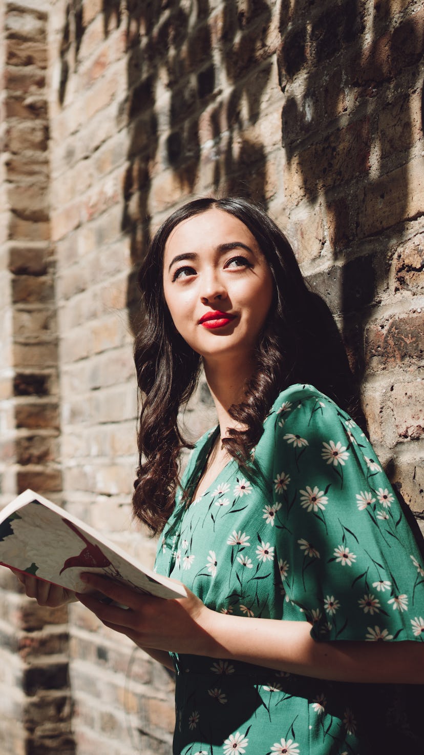 Cheerful beautiful young Asian Brazilian mixed women looking up to the sky while holding a novel on ...