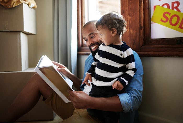 Shot of a young father reading a picture book to his toddler while resting against the window with a...