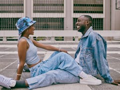 A trendy young Black couple sitting on the ground wearing trendy, baggy denim jeans and a denim jack...