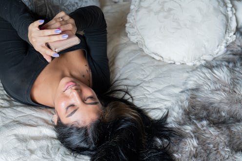 Young latin woman from bogota Colombia between 20 and 24 years old, lying in bed enjoying her cell p...