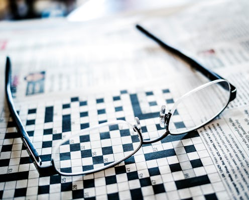 A pair of reading glasses laying across an unfilled newspaper crossword