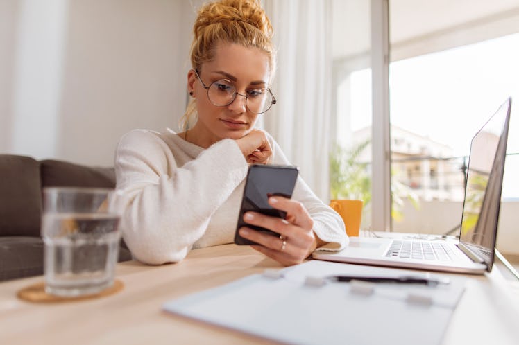 Young blond woman using her cellular phone while working from home
