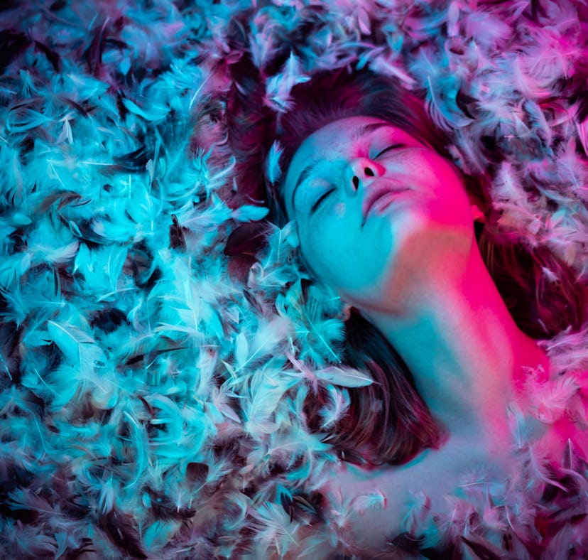Portrait of a young Caucasian woman in feathers with multicolor highlights on her face.