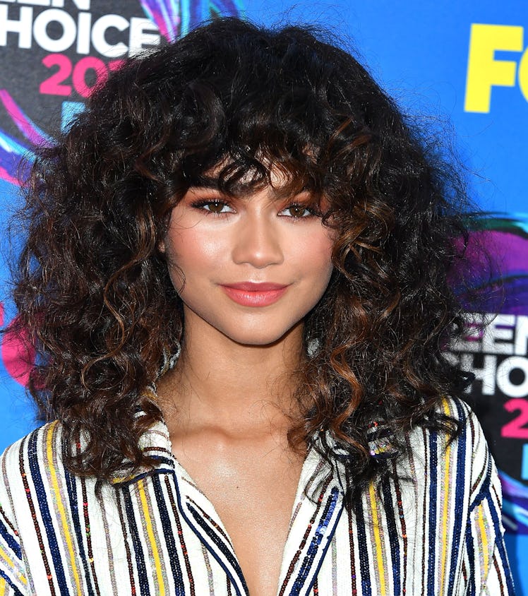 Zendaya posing on the red carpet at the 2017 Teen Choice Awards with a curly shag and curly, shaggy ...