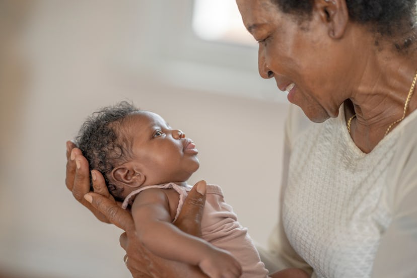 An African American grandmother holds her newborn granddaughter and smiles down at her.