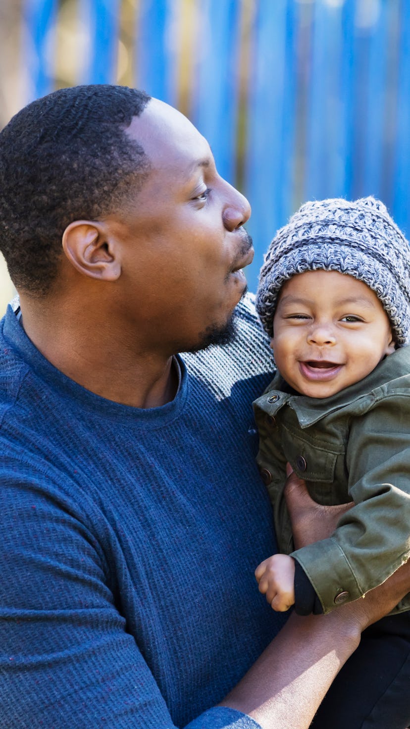 A mixed race father standing on a playground holding his baby boy, playing with him. Dad is a mid ad...