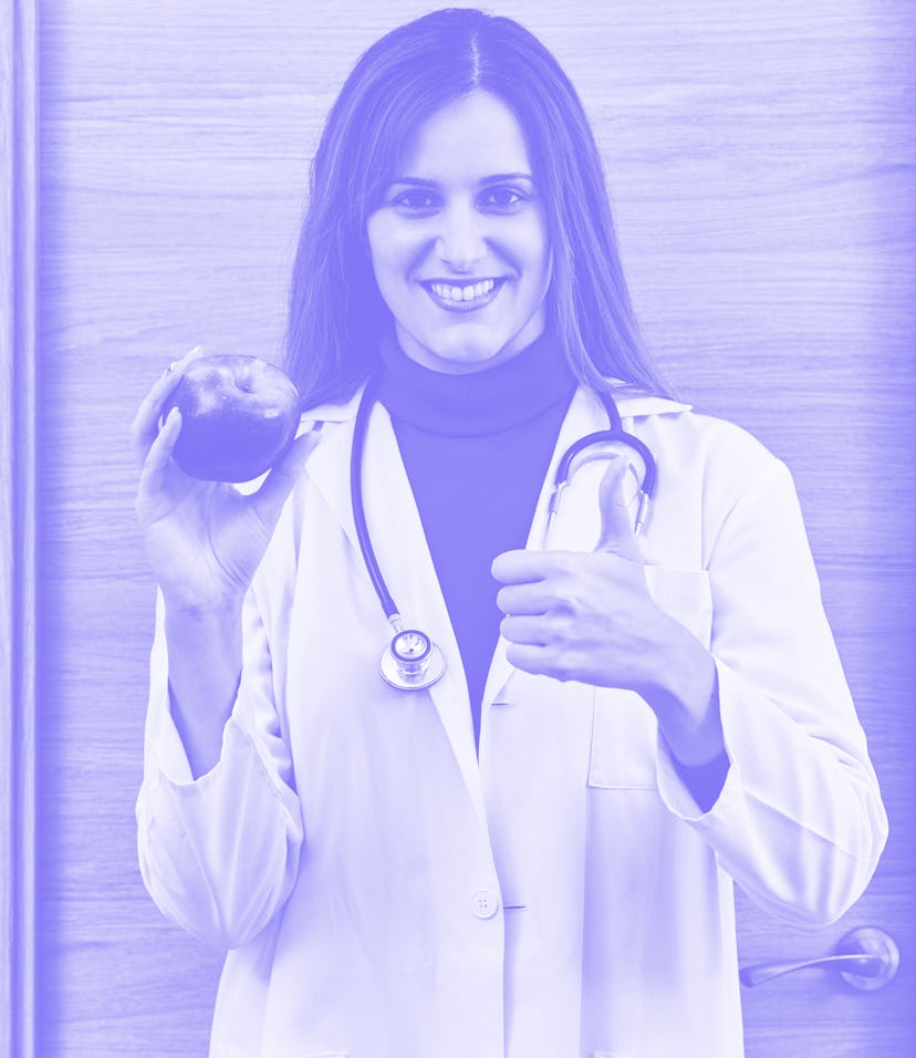 Portrait of young female doctor holding an apple in her hand. Concept of healthy food and nutrition.