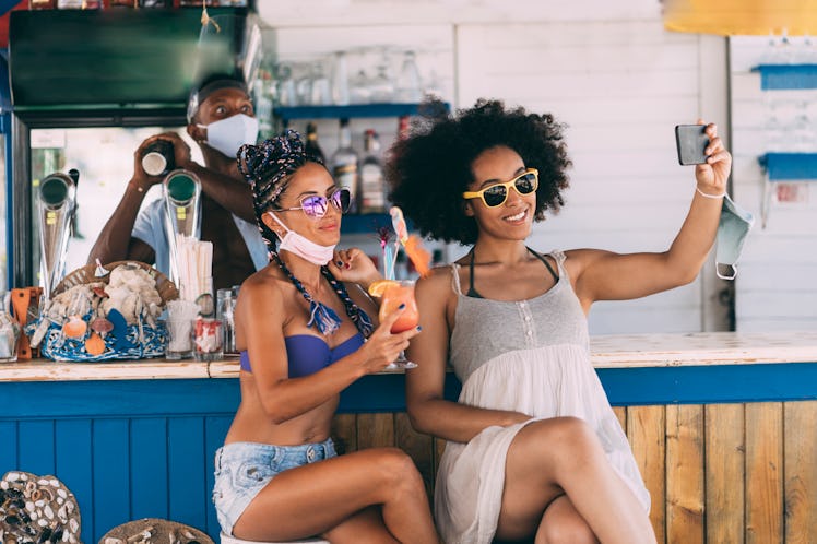Friends taking selfie photos in a summer bar during their vacation in time of coronavirus conditions