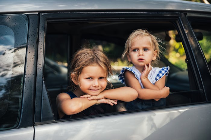 two little girls looking out the window of a parked car