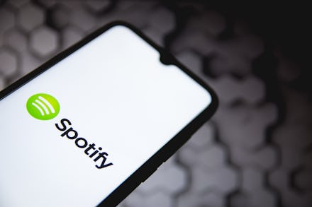 In this photo illustration a Spotify logo seen displayed on a smartphone screen with a computer wall...