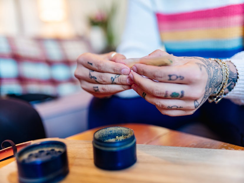 Young woman with tattoos rolls a cannabis joint. Smoking dabs can lead to side effects like increase...