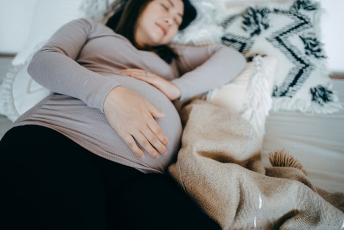 Asian pregnant woman holding her belly, sleeping on bed. Comfortable sleeping positions during pregn...