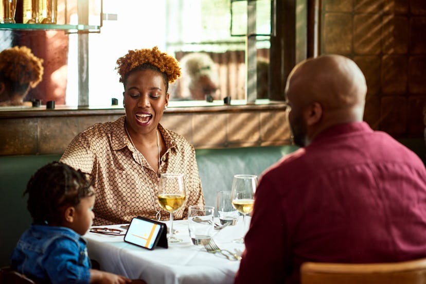 Woman looking at son using smartphone in restaurant, waiting patiently for dinner