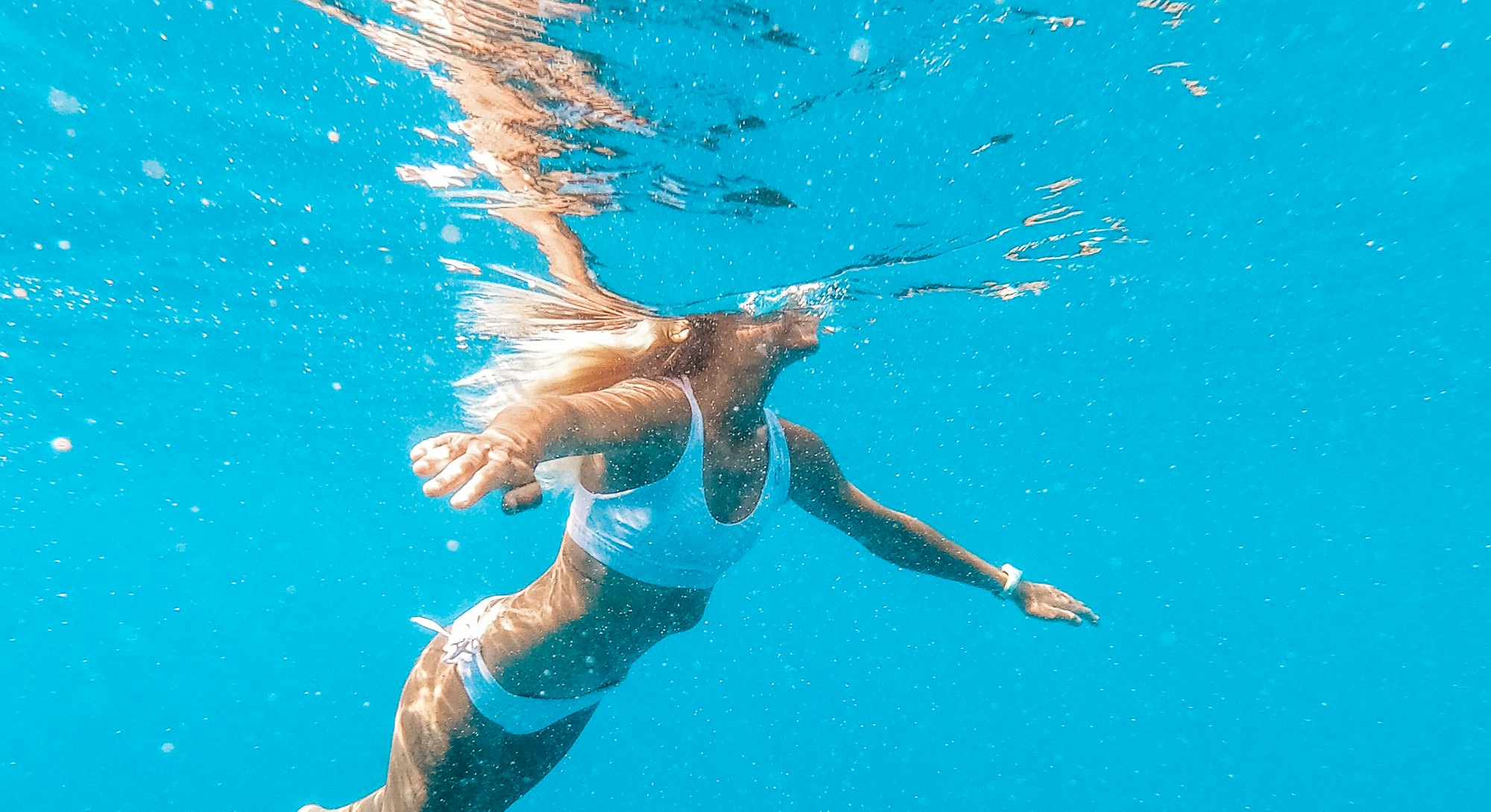 A woman swims underwater. Swimming workout benefits.