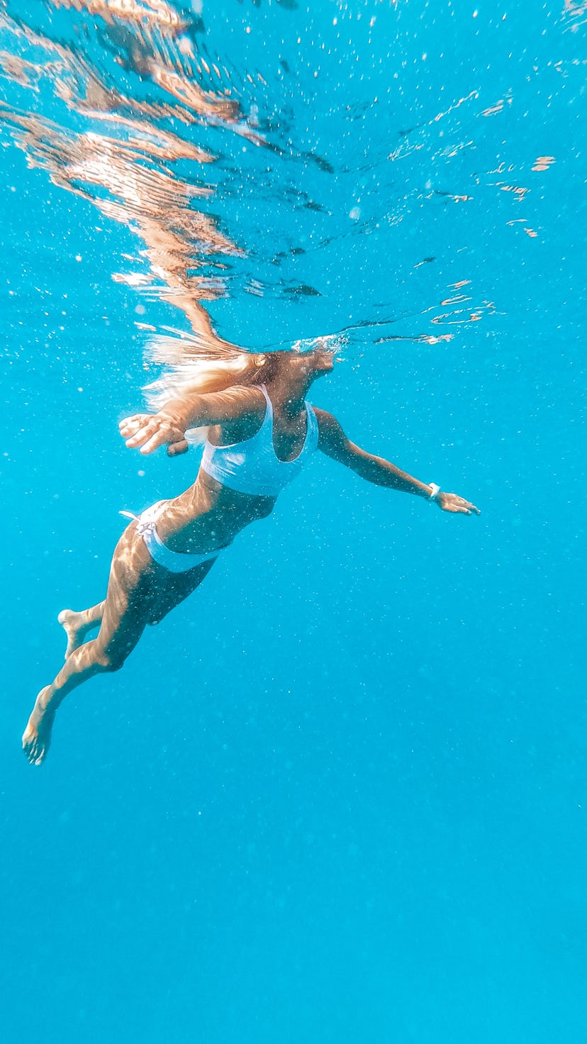 A woman swims underwater. Swimming workout benefits.