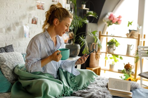 A woman checks her previously liked posts on Instagram while drinking coffee in bed.