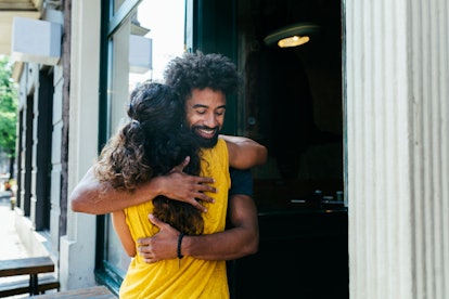 Two friends greeting each other and embracing outside a restaurant.