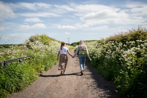 A rear-view shot of an LGBTQIA female couple walking down a country footpath together, they are wear...