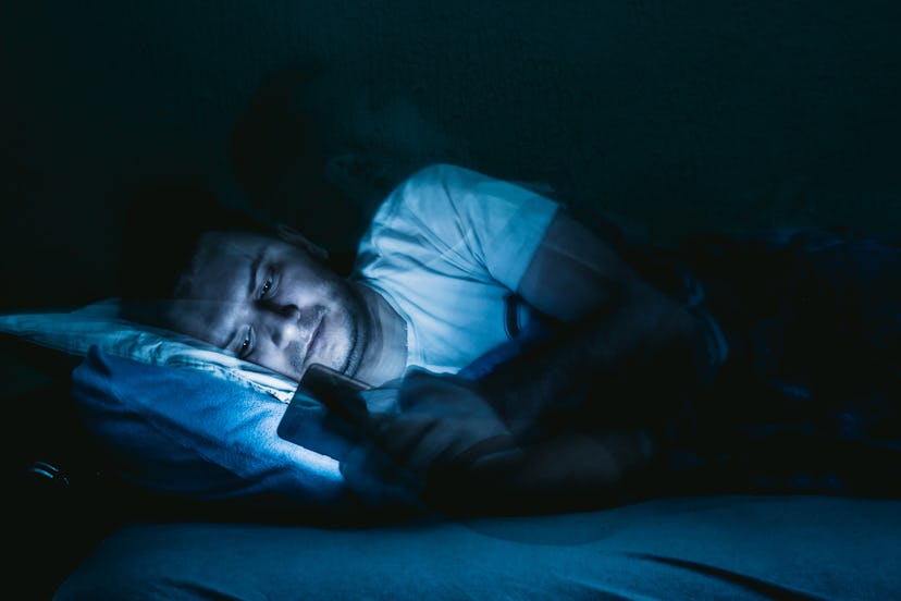 Man lying in bed and using smartphone. Spending time during pandemic lockdown. Coronavirus/Covid-19.