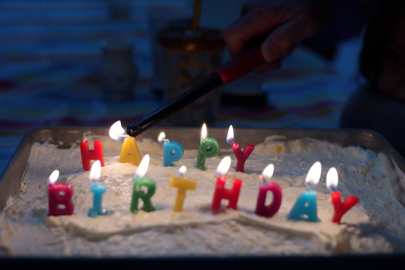 Close-up view of top of cake with colorful letters. Happy birthday inscription made of wax. Igniting...