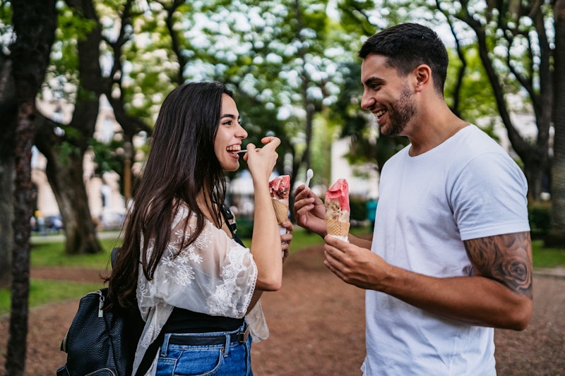 Young smiling cute heterosexual couple eating ice cream in public park and having good time.