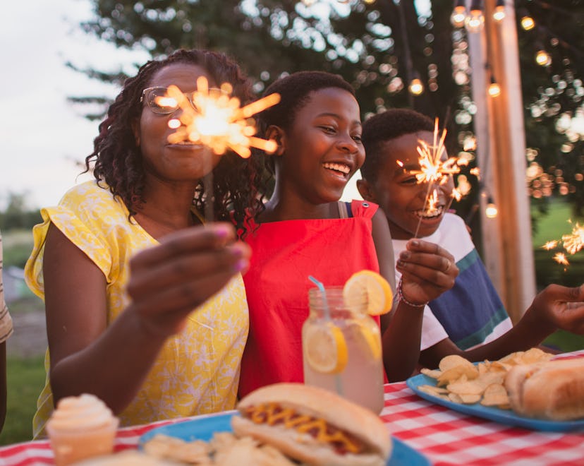 A family sits at a table outside and enjoys a summer barbecue together. fourth of july instagram cap...