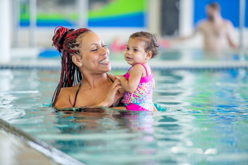 A person smiles while holding their child in a swimming pool. Swimming can be accessible to people o...