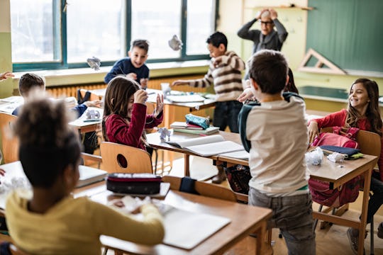 Large group of school kids making chaos during a class in the classroom while their teacher is frust...