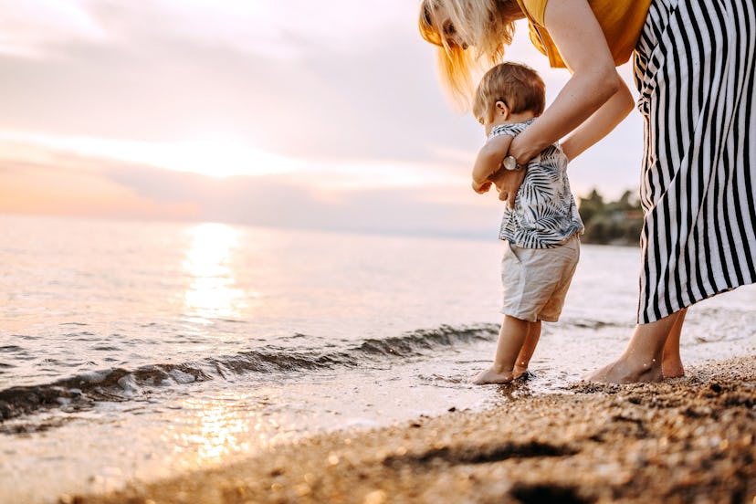 Young mother with little boy enjoying walking in the sea at the sunset