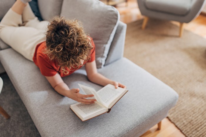 One woman, beautiful young woman lying on sofa at home, she is reading a book.