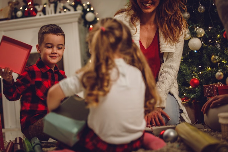 Selective focus shot of two little kids sitting on the floor, under the Christmas tree and opening p...