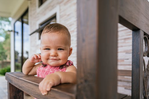 Beautiful baby sitting in a wooden chair on the terrace making funny faces.