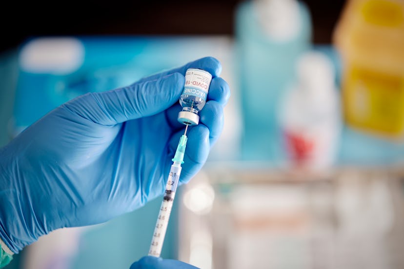 A healthcare Worker hands in surgical gloves pulling COVID-19 vaccine liquid from vial to vaccinate ...