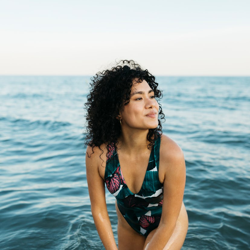 Young woman wearing swimsuit in the sea, smiling while the July 2021 new moon affects her the most.