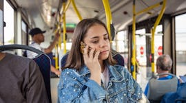 Teenage girls talking on mobile phone in bus. Female passenger is traveling in public transport. She...