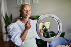 Young African female influencer showing how to apply lip gloss while doing a vlog post from home usi...