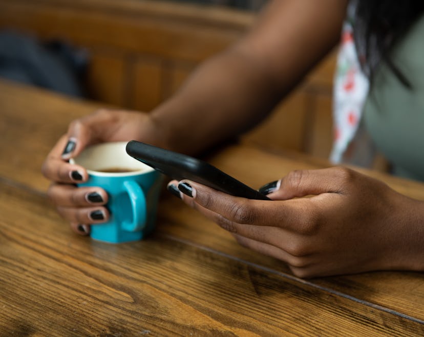 Young woman sitting at a wooden kitchen table, texting on her phone