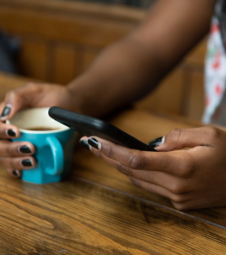 Young woman sitting at a wooden kitchen table, texting on her phone