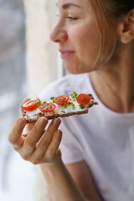 A woman eats an open faced sandwich to avoid low blood sugar, a common reason for sweating when cold