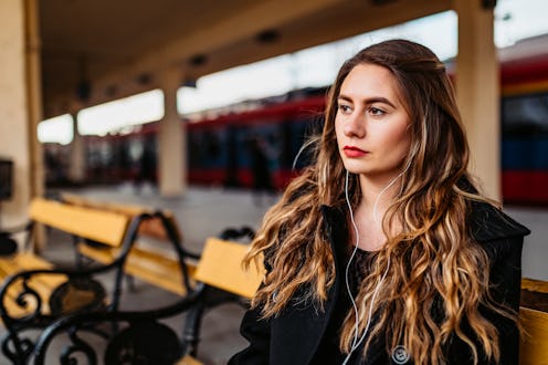 Young Caucasian beautiful woman listening music on her phone while waiting for a train on railroad s...