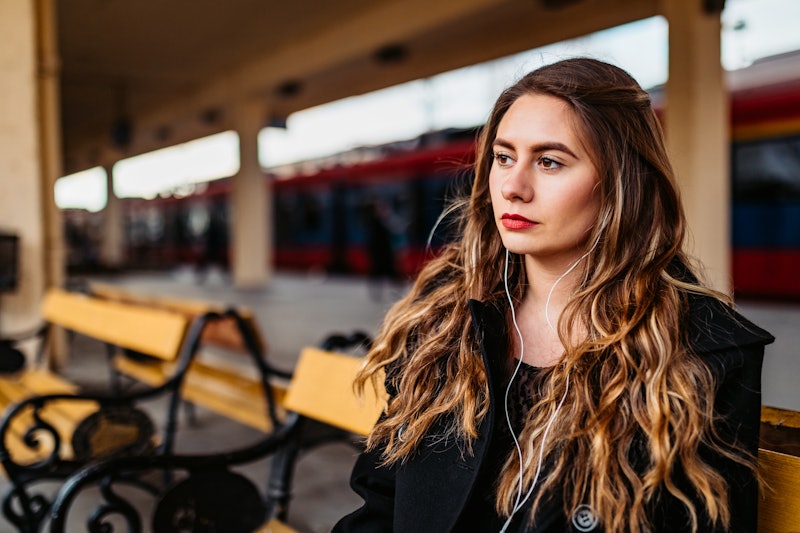 Young Caucasian beautiful woman listening music on her phone while waiting for a train on railroad s...