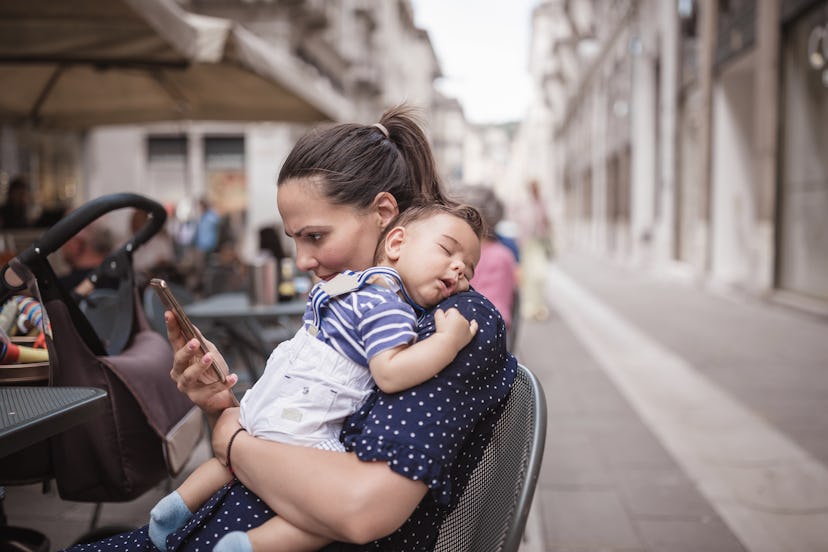Young mother holding baby boy while on phone